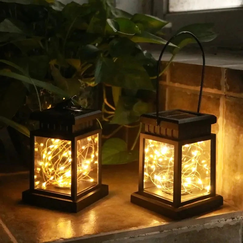 Two solar garden lanterns with warm white LED lights, one with hanging hook, on a tiled windowsill