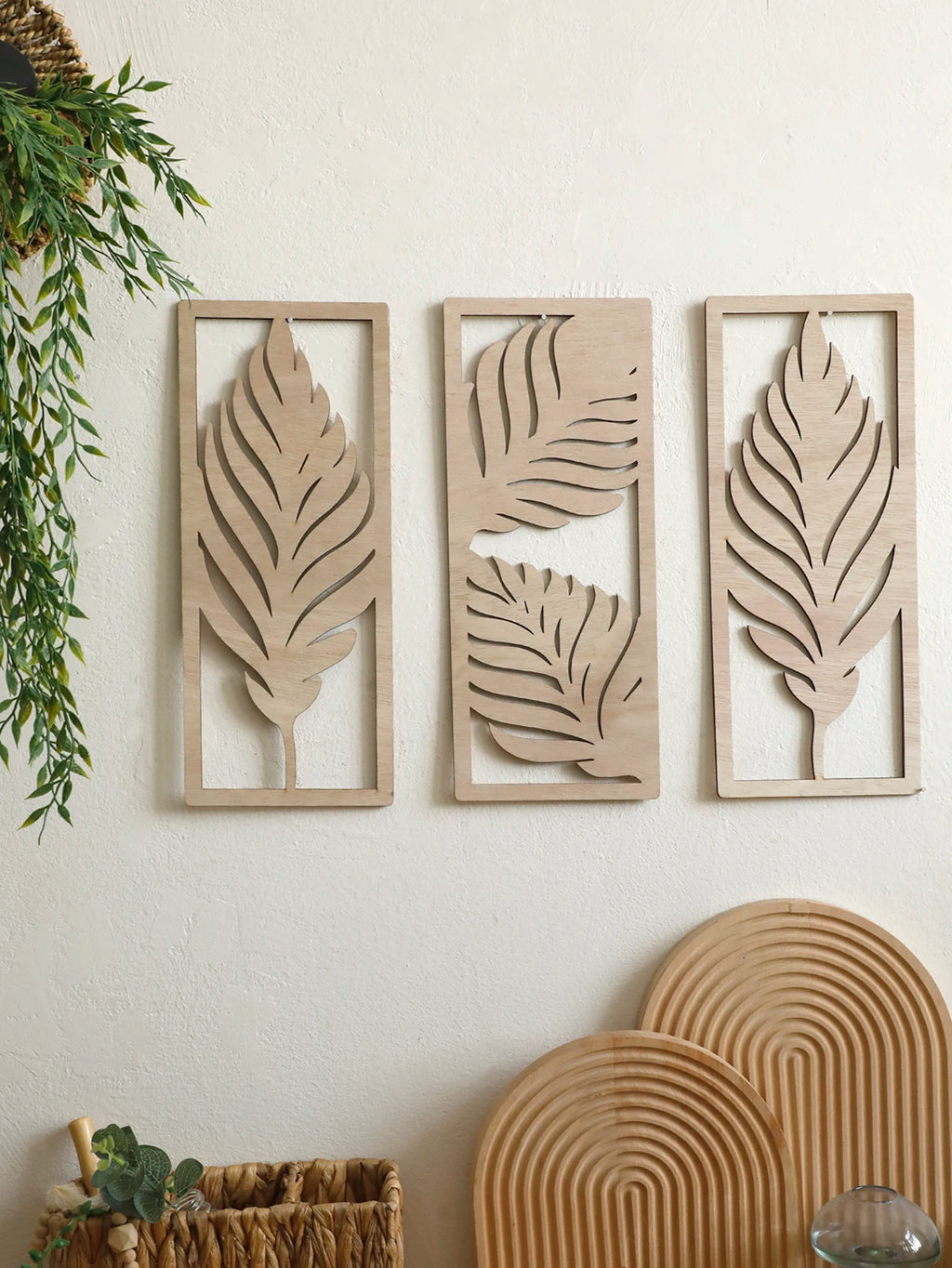 Three rectangular wooden palm leaf wall art panels arranged together above a basket and decor
