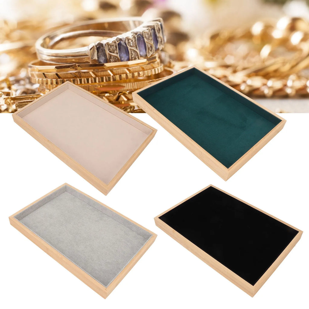 Set of four wood and velvet jewelry trays in beige, gray, black, and green arranged on a background of jewelry