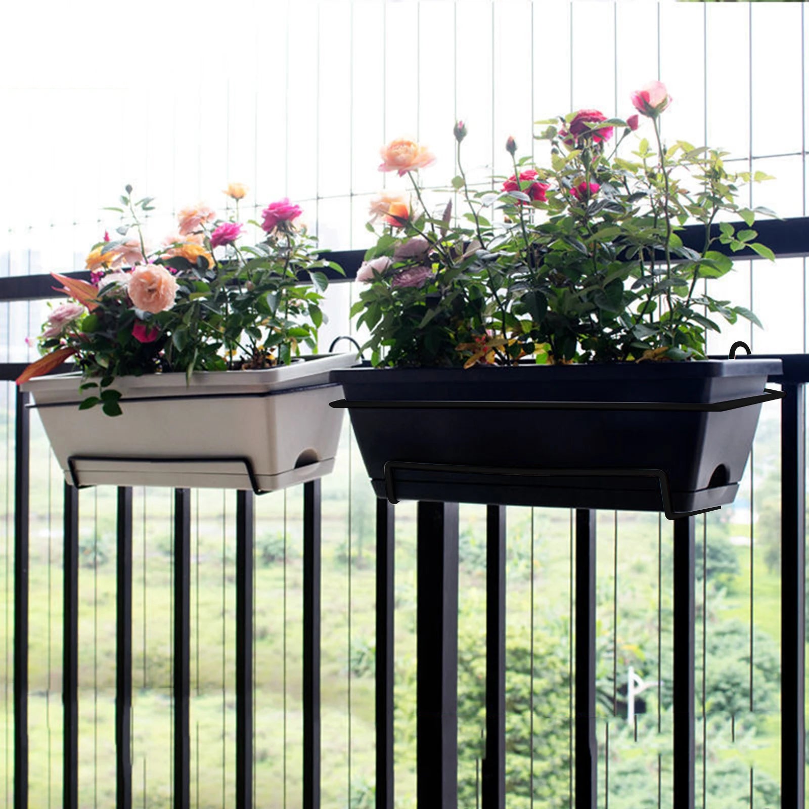 Two rectangular railing planter boxes, one white and one black, filled with blooming flowers on a metal balcony railing