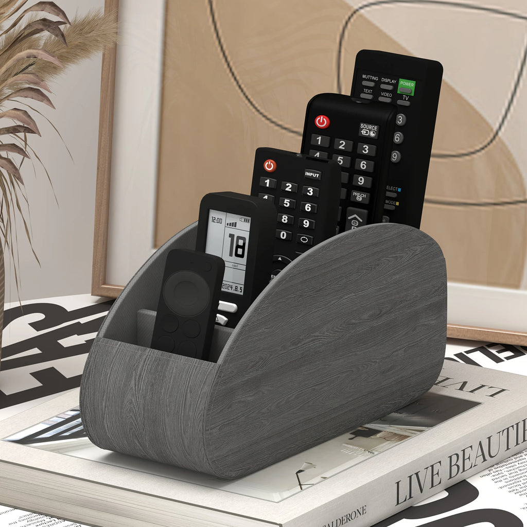 Gray remote control caddy with remotes, placed on a stack of magazines in a cozy room setting