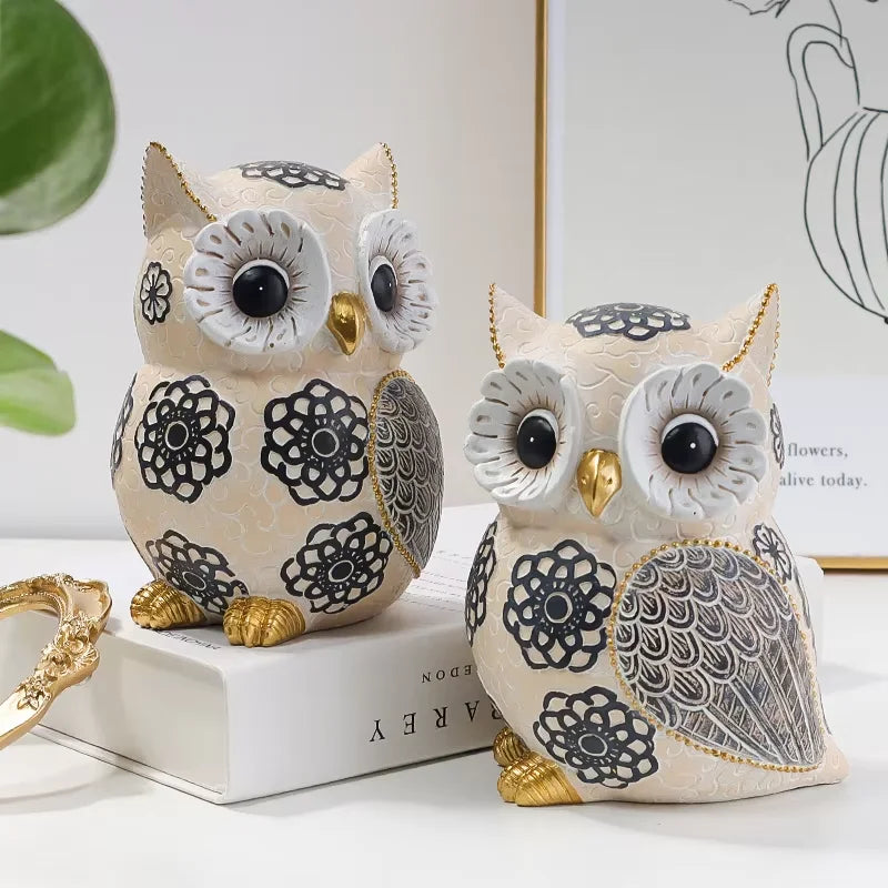 two whimsical owl sculptures side by side on a shelf with gold and floral details