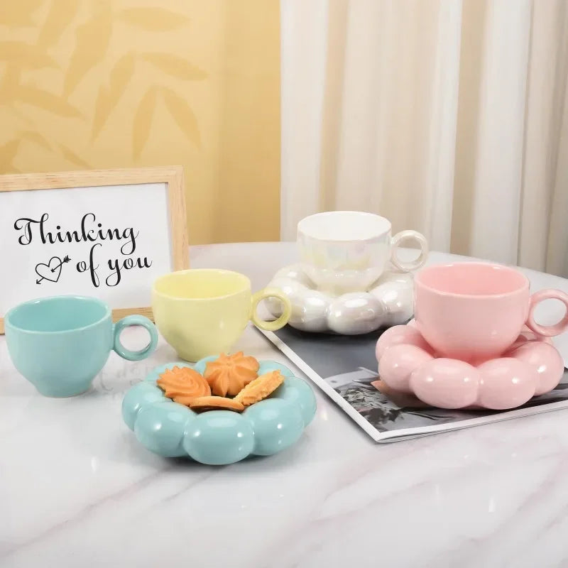 Pastel yellow, blue, white, and pink cloud ceramic cups and saucers displayed next to cookies and a 'Thinking of you' sign