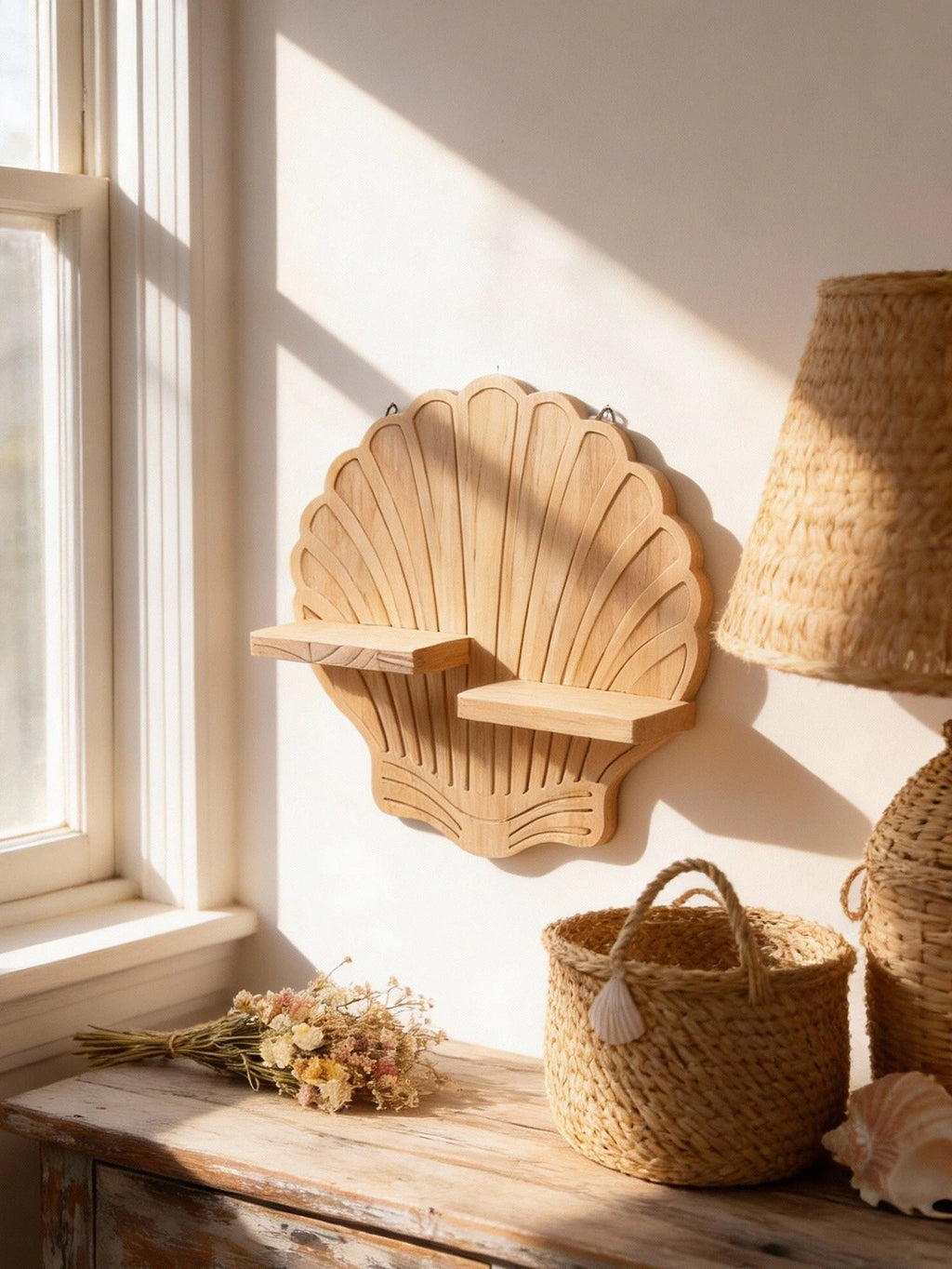 Seashell-shaped wooden wall shelf mounted above a rustic dresser with woven basket, dried flowers, and sunlight streaming in—a natural coastal accent.
