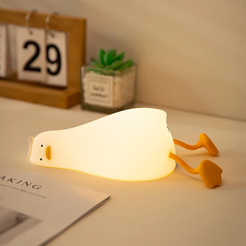 Cute lying duck night light with soft white body and yellow feet on a tabletop