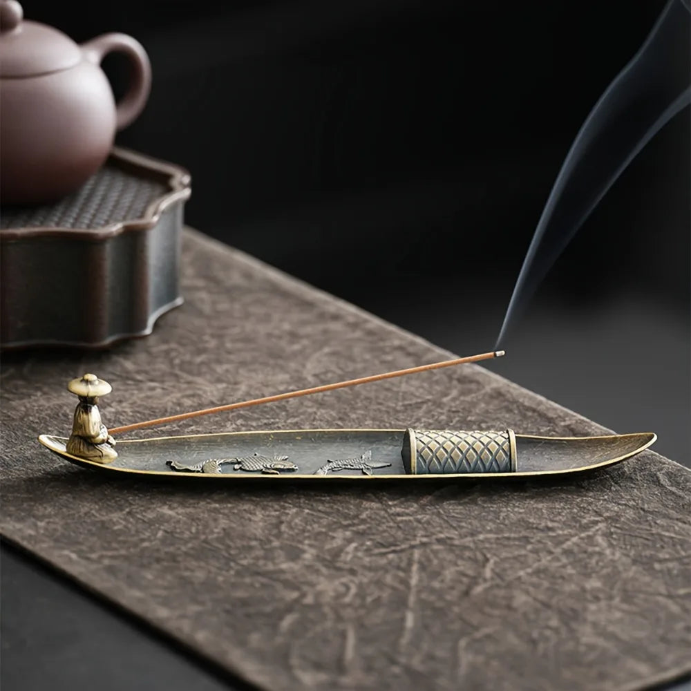 Boat-shaped alloy incense stick holder with fisherman figure, shown on a table with incense burning