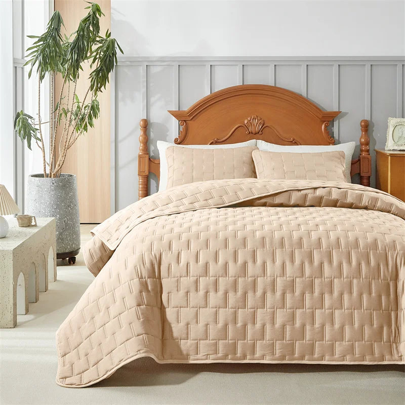 Beige quilted bedspread and shams styled in a cozy bedroom with wood headboard