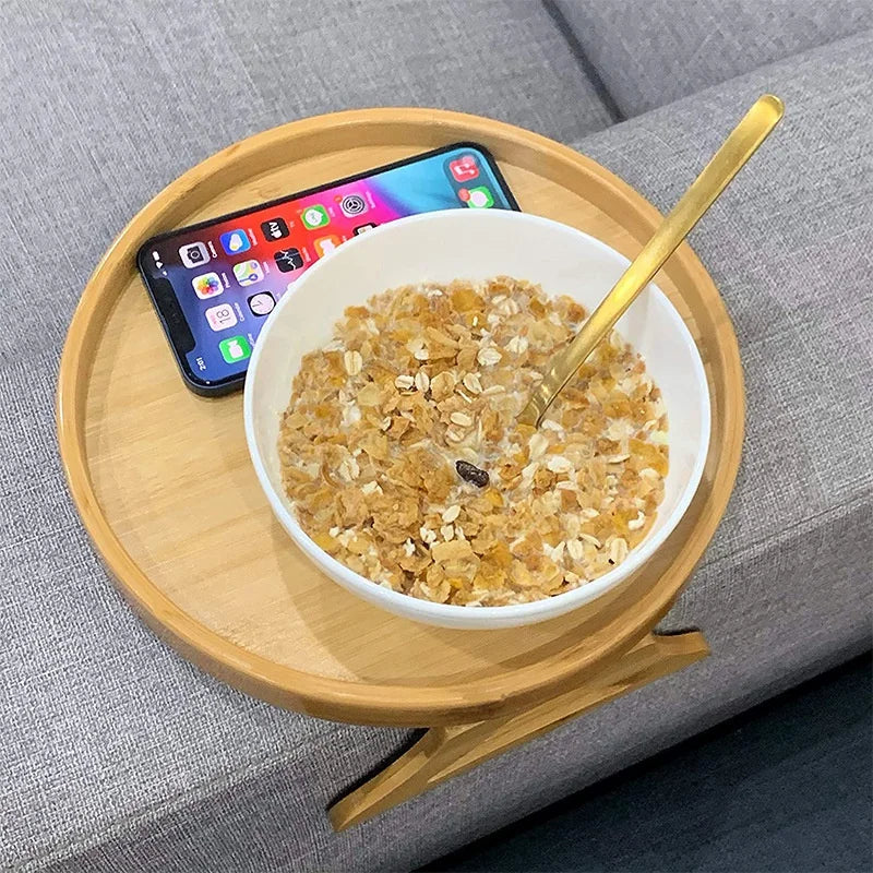 Bamboo sofa armrest tray holding a bowl of cereal with a spoon and a smartphone