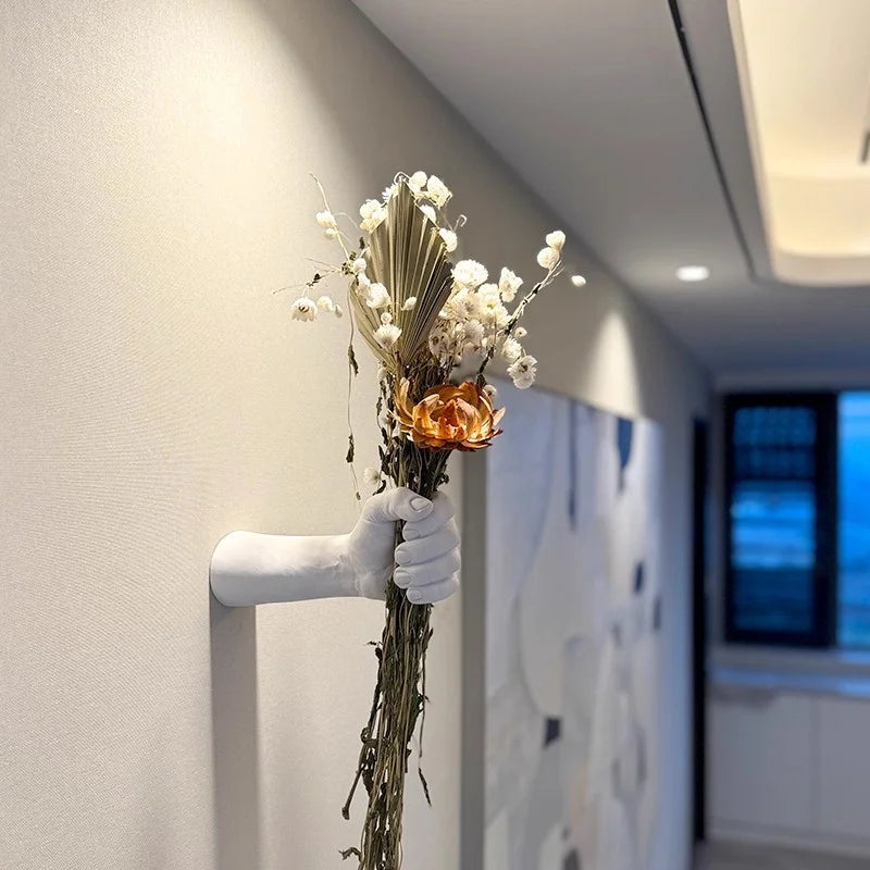 Fist-shaped wall vase holding dried flowers in a hallway setting