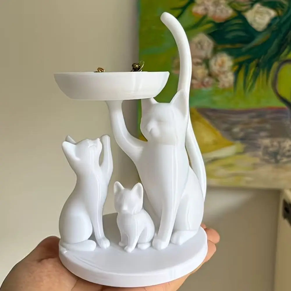White cat family jewelry tray displayed in hand with a painting background