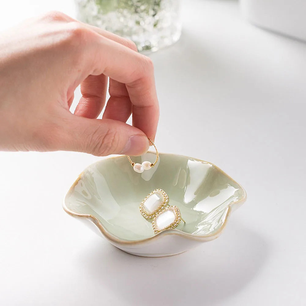 Light green ceramic petal jewelry tray on white, with a hand placing a ring and other jewelry inside