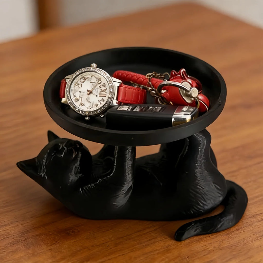 Black cat-shaped decorative jewelry tray with watch, keys, and small items on a wooden table