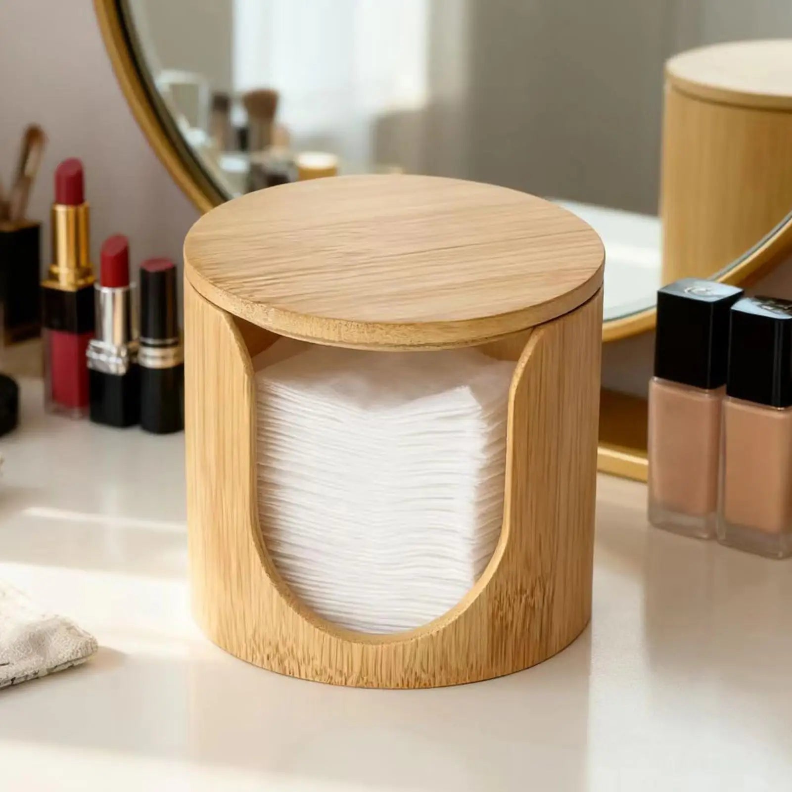Round bamboo cotton pad holder with lid on a vanity table next to makeup essentials