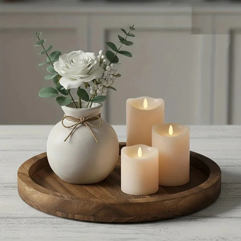 Solid wood round decorative tray on a table, holding a small vase with white flowers and three ivory pillar candles