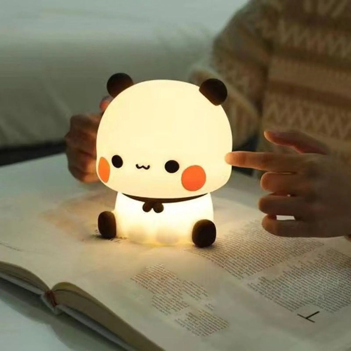 Bear silicone LED night light sitting on an open book, glowing warmly for reading or bedtime