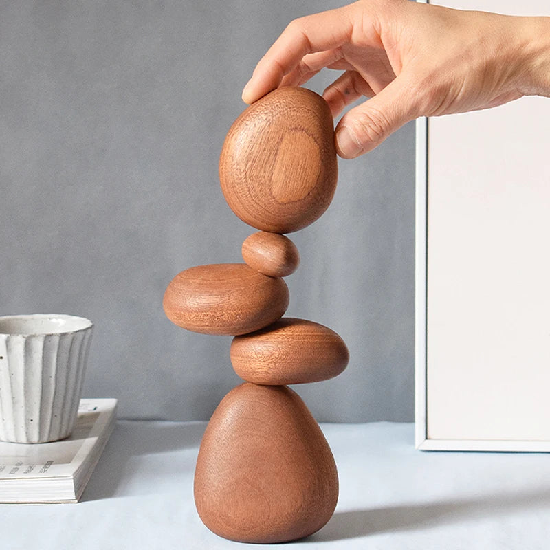 Hand placing stone piece on stacking wooden sculpture beside a mug