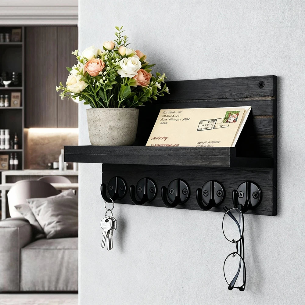 Black wooden wall-mounted key and mail holder with five hooks, shelf holding a plant and mail, styled in an entryway.