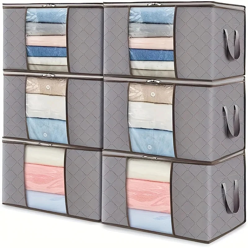 Six gray extra large foldable storage bags stacked with folded clothes and blankets inside, handles on the sides and clear window panels on the front.