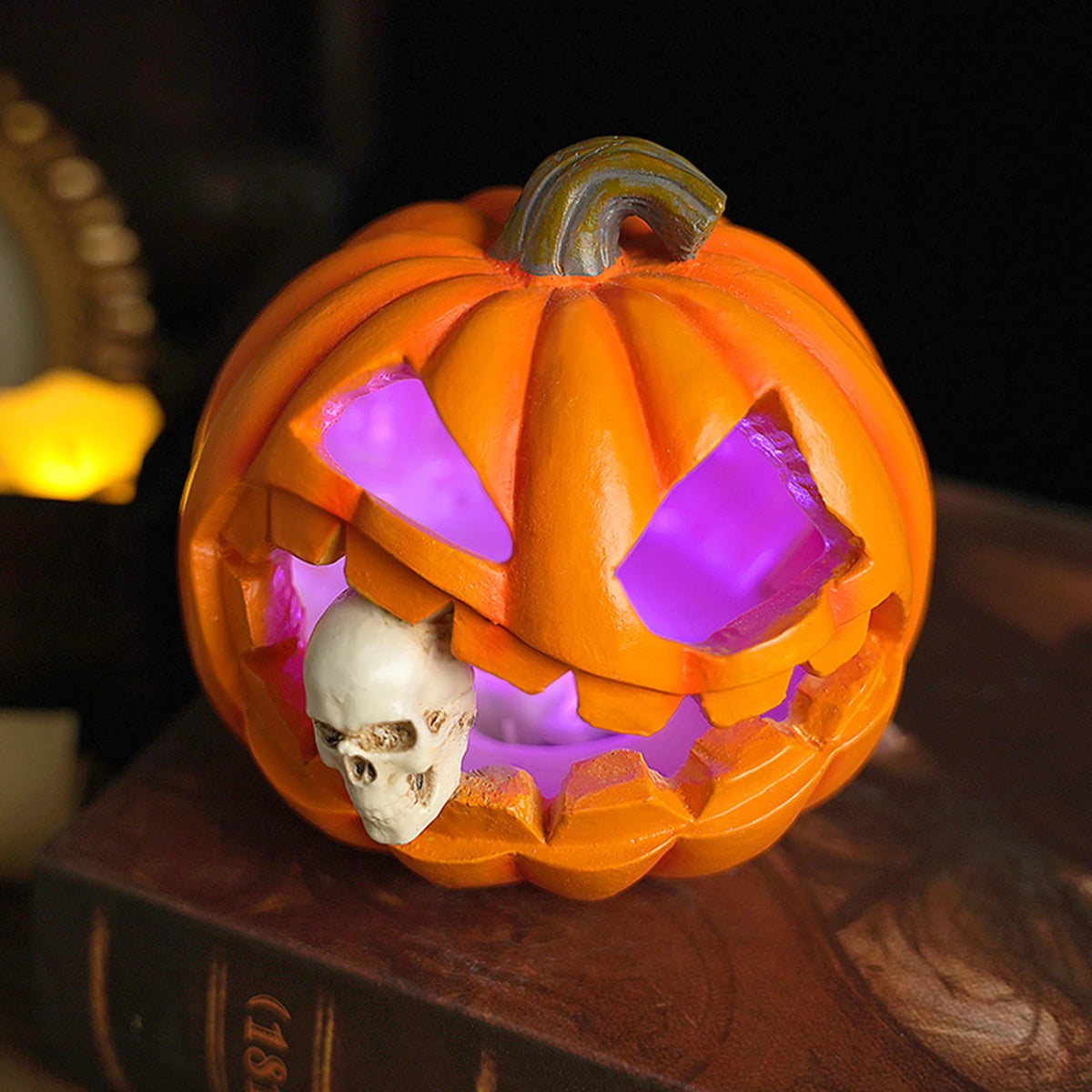 compact resin pumpkin lantern with carved face and skull, placed on a book
