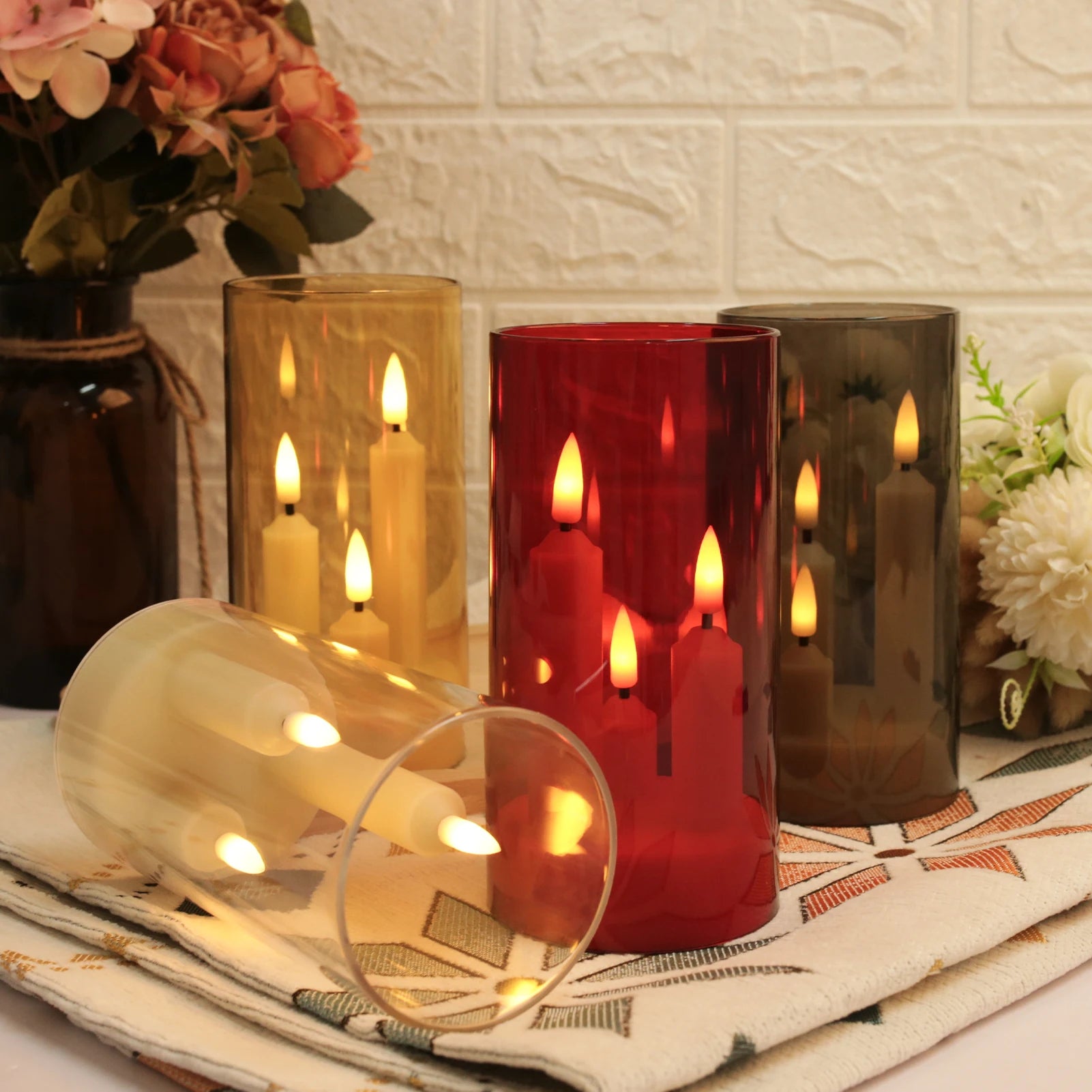 Four flameless LED taper candle trios in gold, red, grey, and transparent cylinder shades displayed together on a table