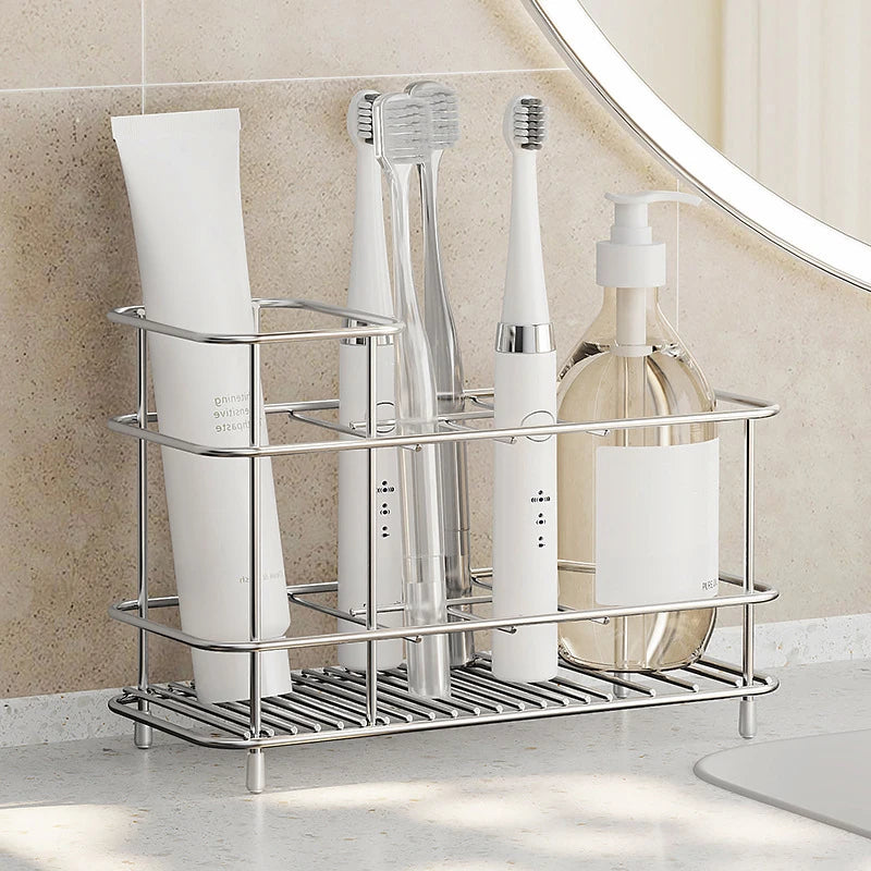 Stainless steel toothbrush holder on bathroom countertop, holding toothbrushes, toothpaste, and a pump bottle