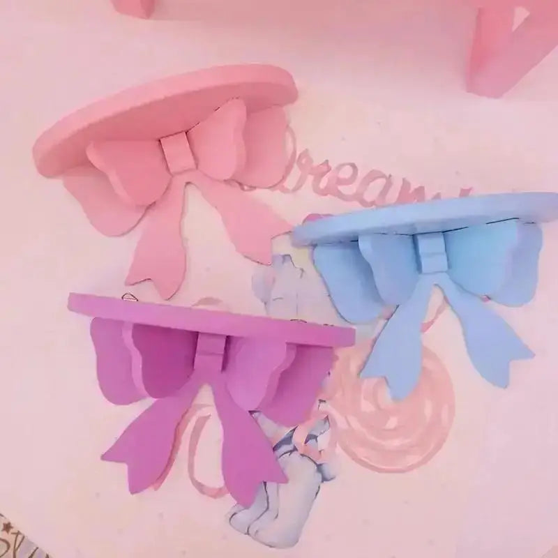 Three pastel bow-shaped wooden wall shelves for kids room in pink, blue, and purple