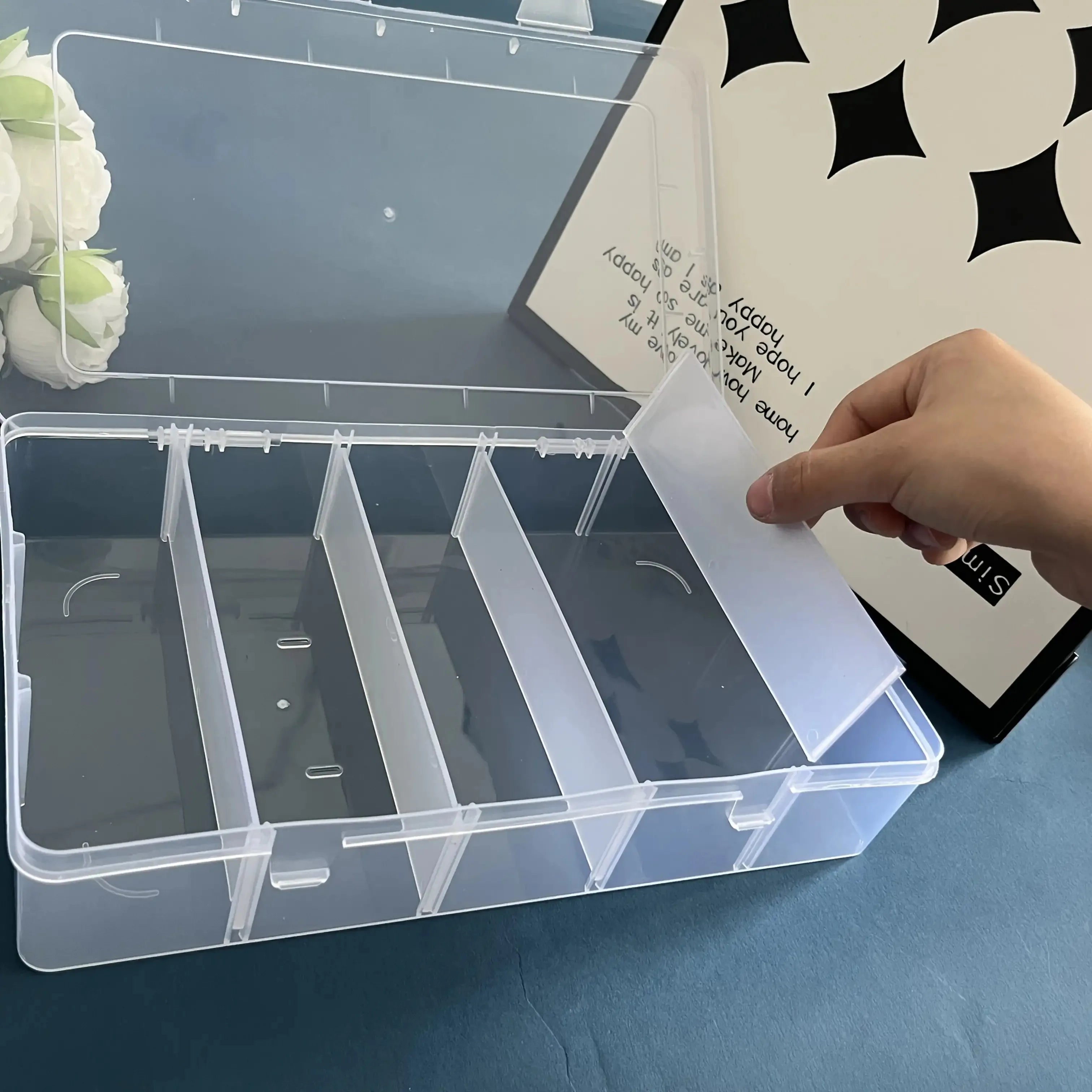 Person adjusting removable divider in empty clear organizer box on blue table