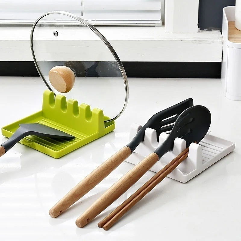 Green and white kitchen utensil rests on counter holding spatulas, spoon, chopsticks, and a pot lid