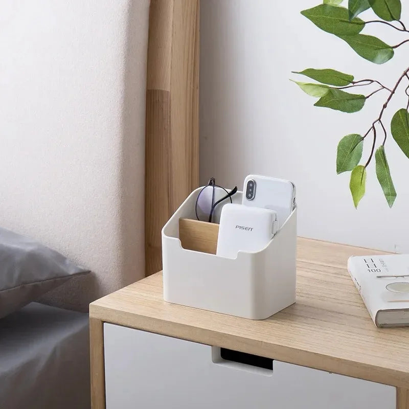 White divider organizer box on a nightstand holding phone, glasses, and small items beside a bed.