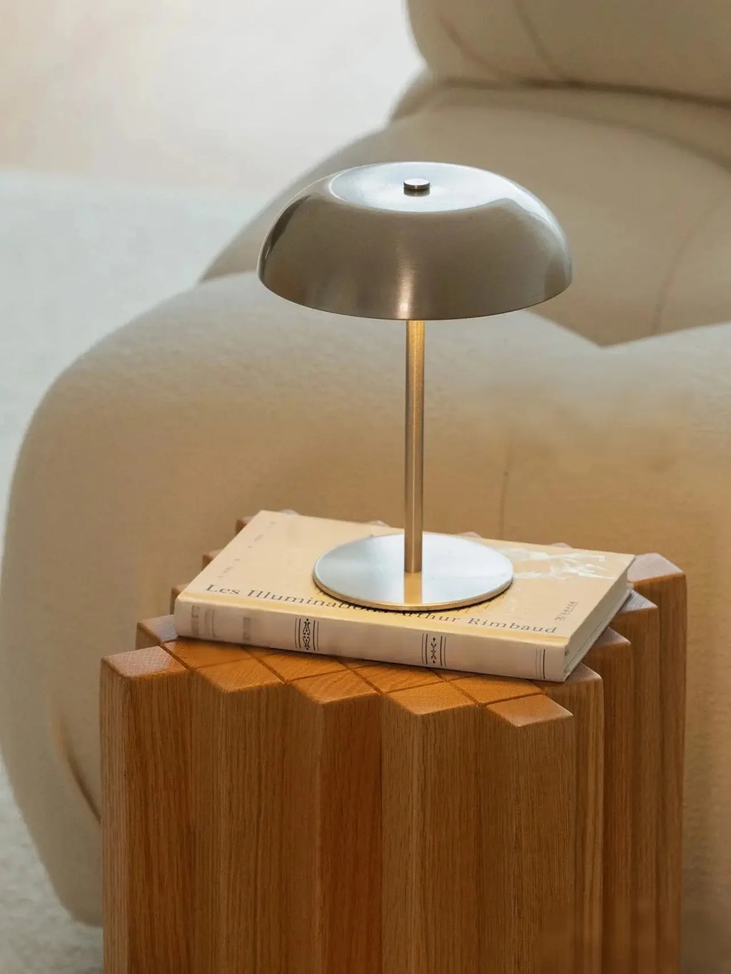 Cordless table lamp in silver on a wood side table beside a cream accent chair