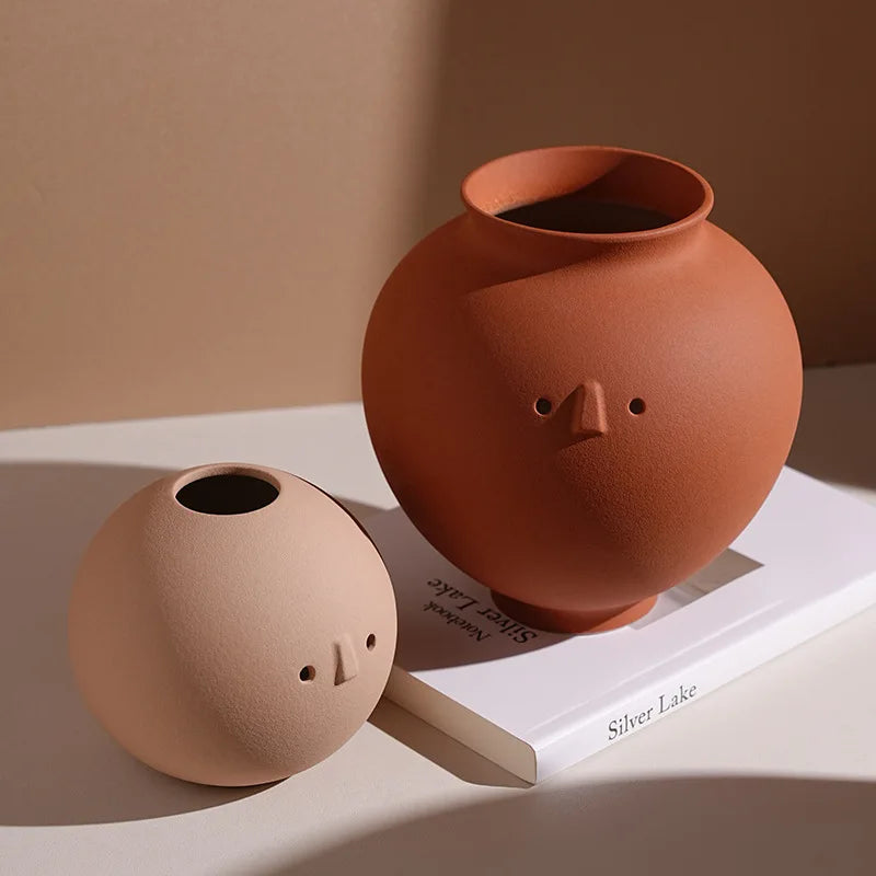 Two modern ceramic face vases, one beige and one terracotta, displayed on a book