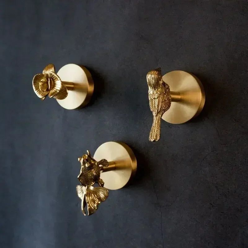 Three brass botanical and bird wall hooks mounted on a dark wall