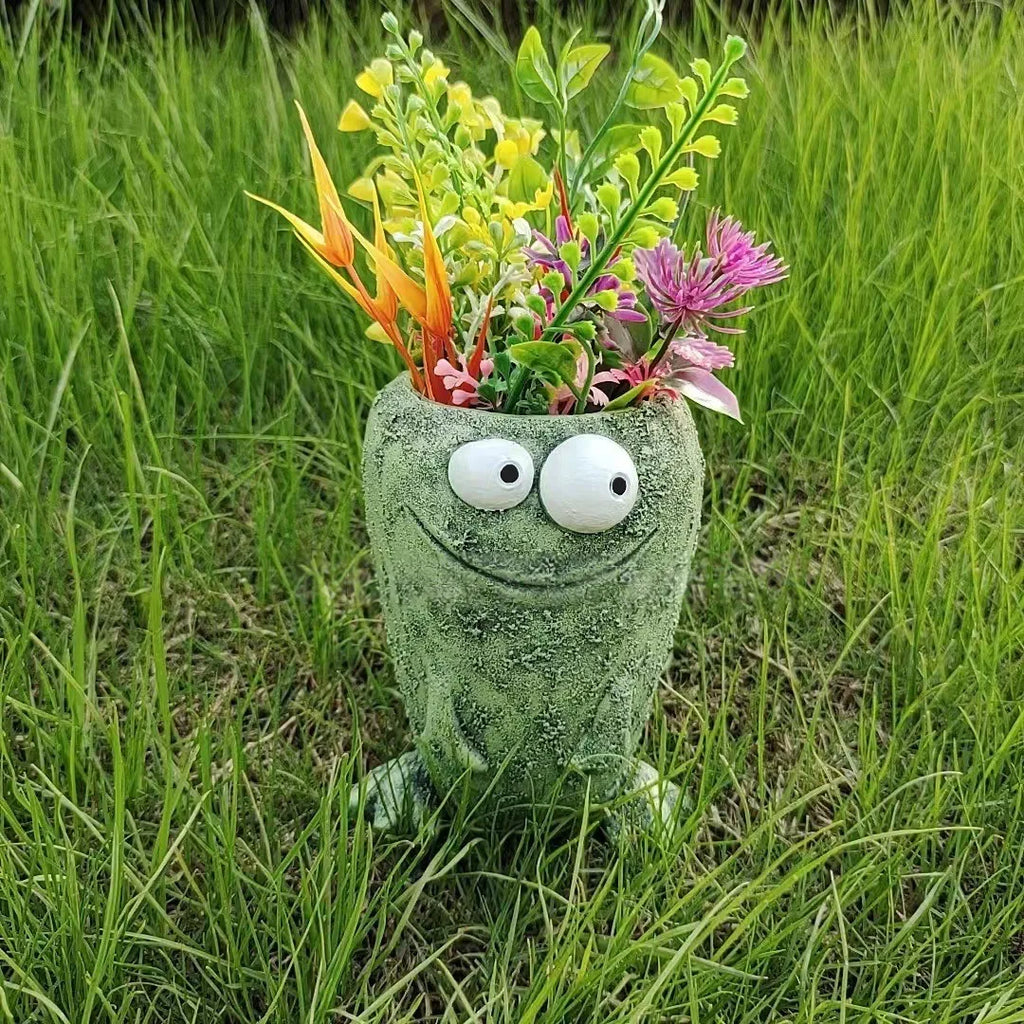 Green smiling frog resin planter with flowers in grassy outdoor setting