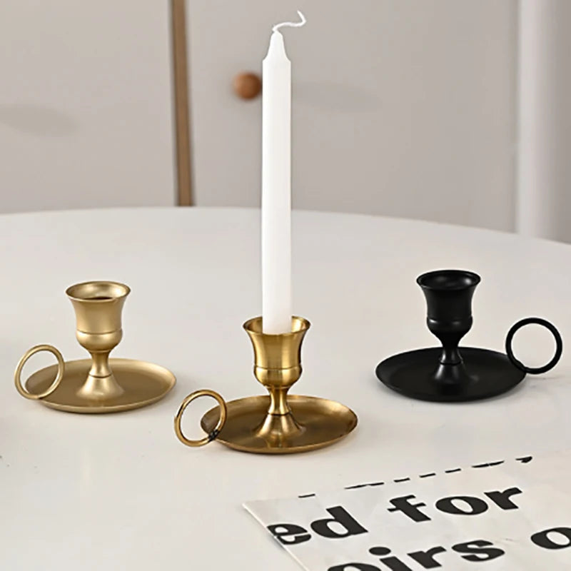 Gold, light gold, and black metal chamberstick candle holders on a white table, one holding a white taper candle