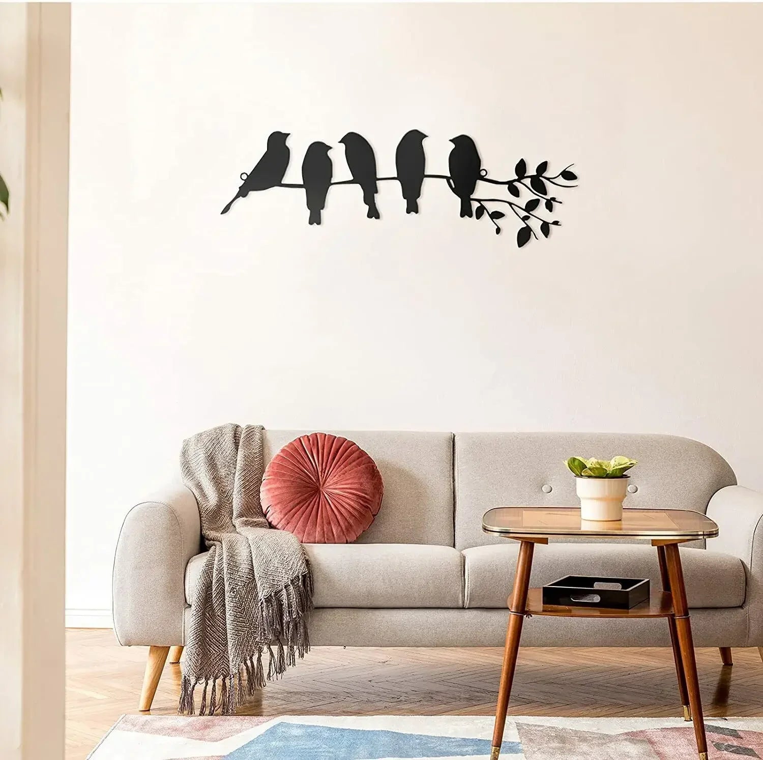 Black metal wall art featuring five birds on a branch, mounted above a modern living room sofa.