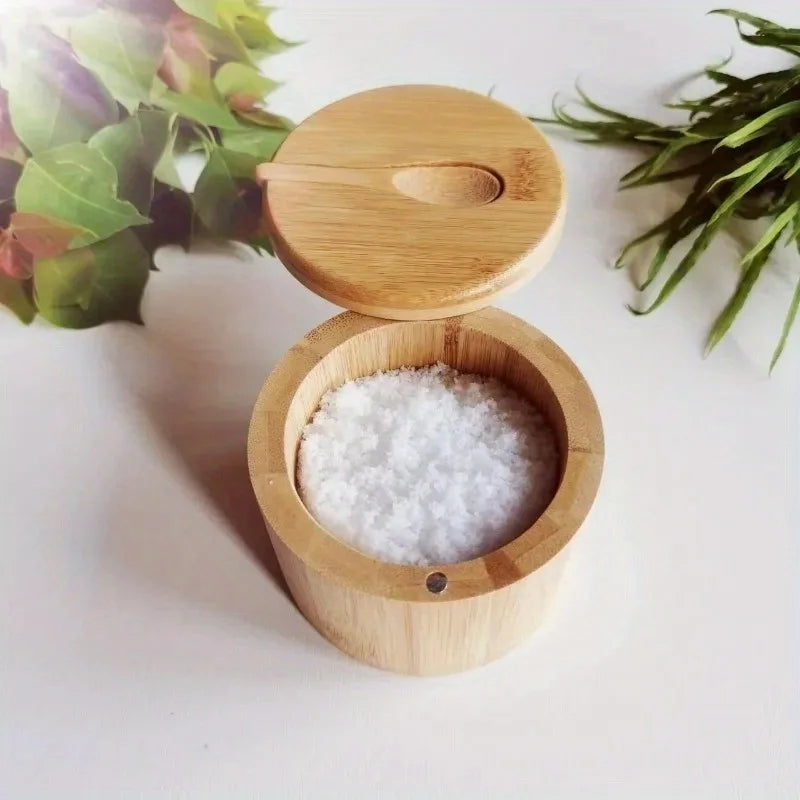 Bamboo salt cellar with lid open, filled with salt, styled near kitchen herbs