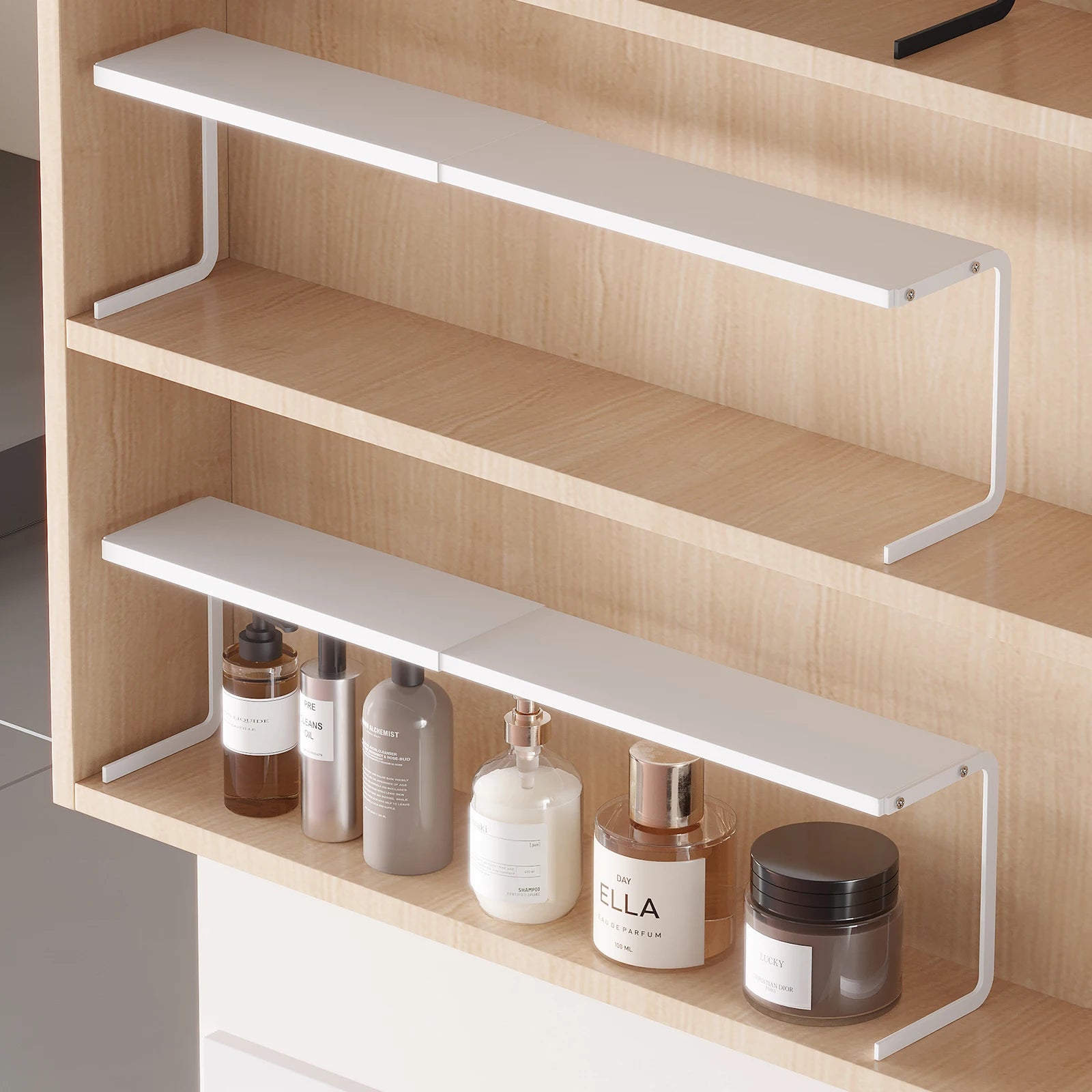 White expandable under-shelf organizer in a bathroom cabinet holding bottles and jars
