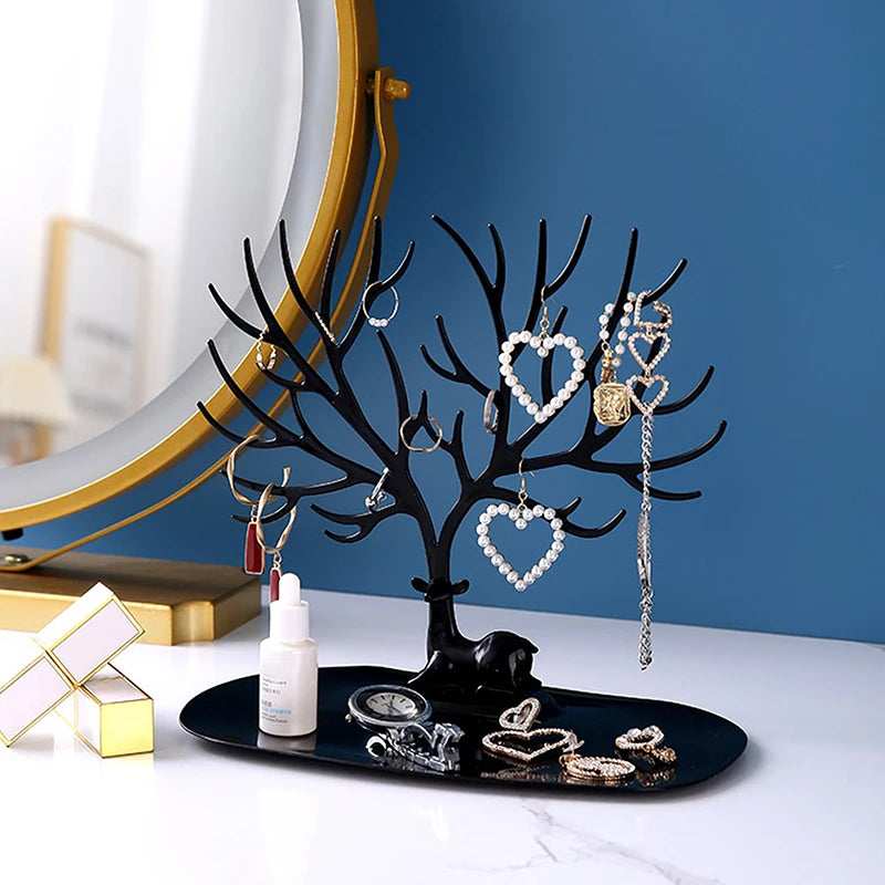 Black reindeer jewelry stand with tray on a white vanity in front of a mirror, displaying hanging earrings and bracelets