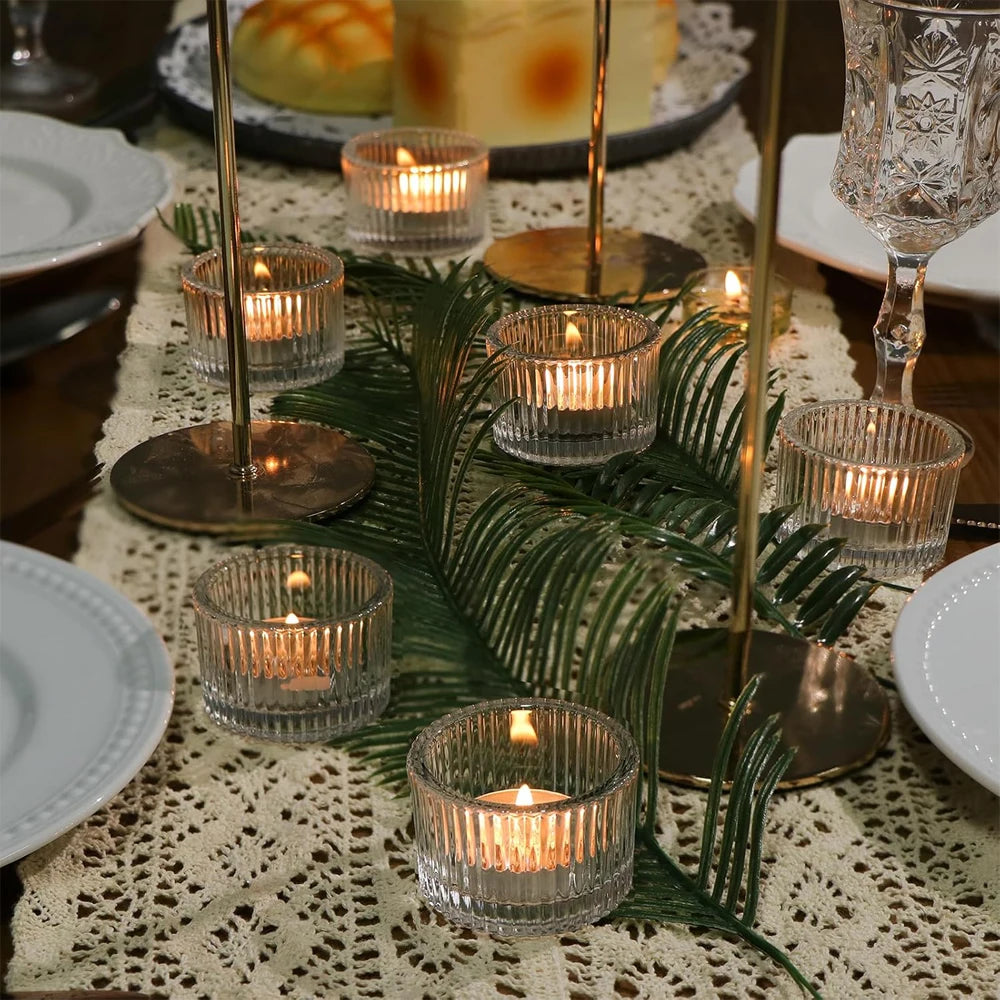 clear glass tealight holders with lit candles arranged on a lace table runner and greenery centerpiece