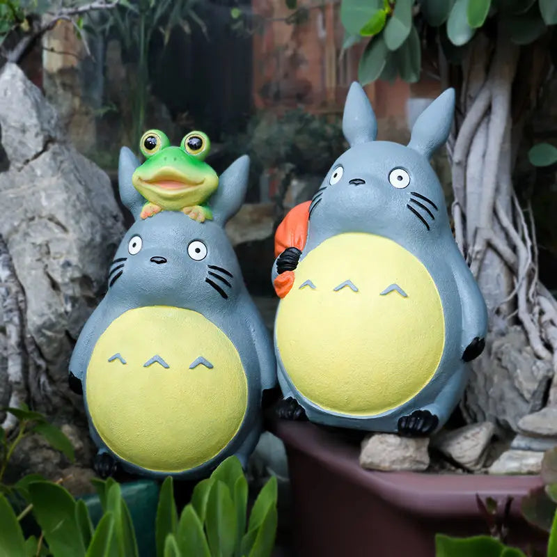 Resin forest animal statues, one with a frog on its head, among garden plants