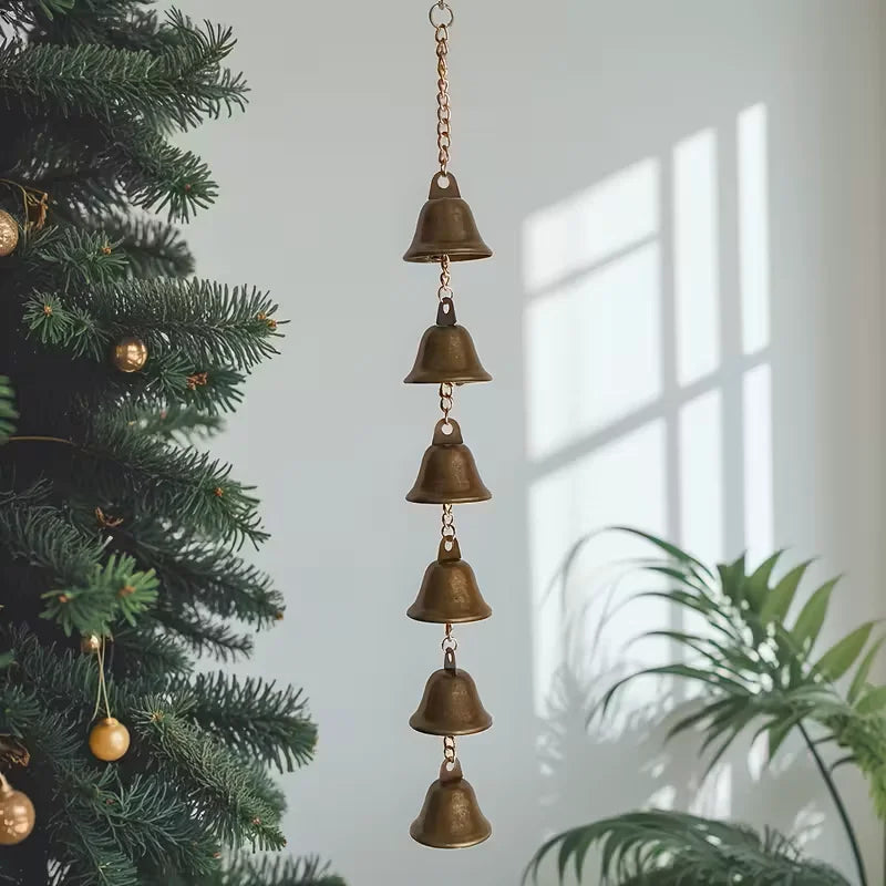 Iron wind chime with multiple bells hanging indoors near a Christmas tree and houseplants