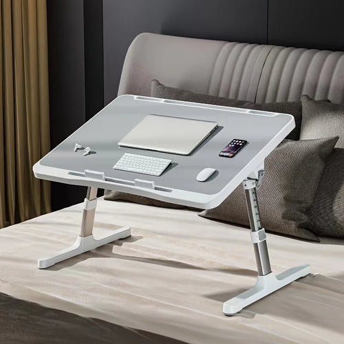 Gray adjustable lap desk placed on a bed, holding a laptop, keyboard, mouse, and phone