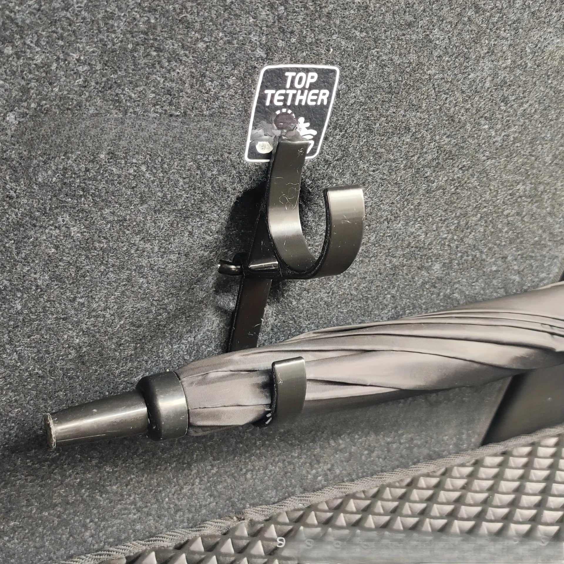 Car trunk umbrella hook installed on top tether point holding an umbrella