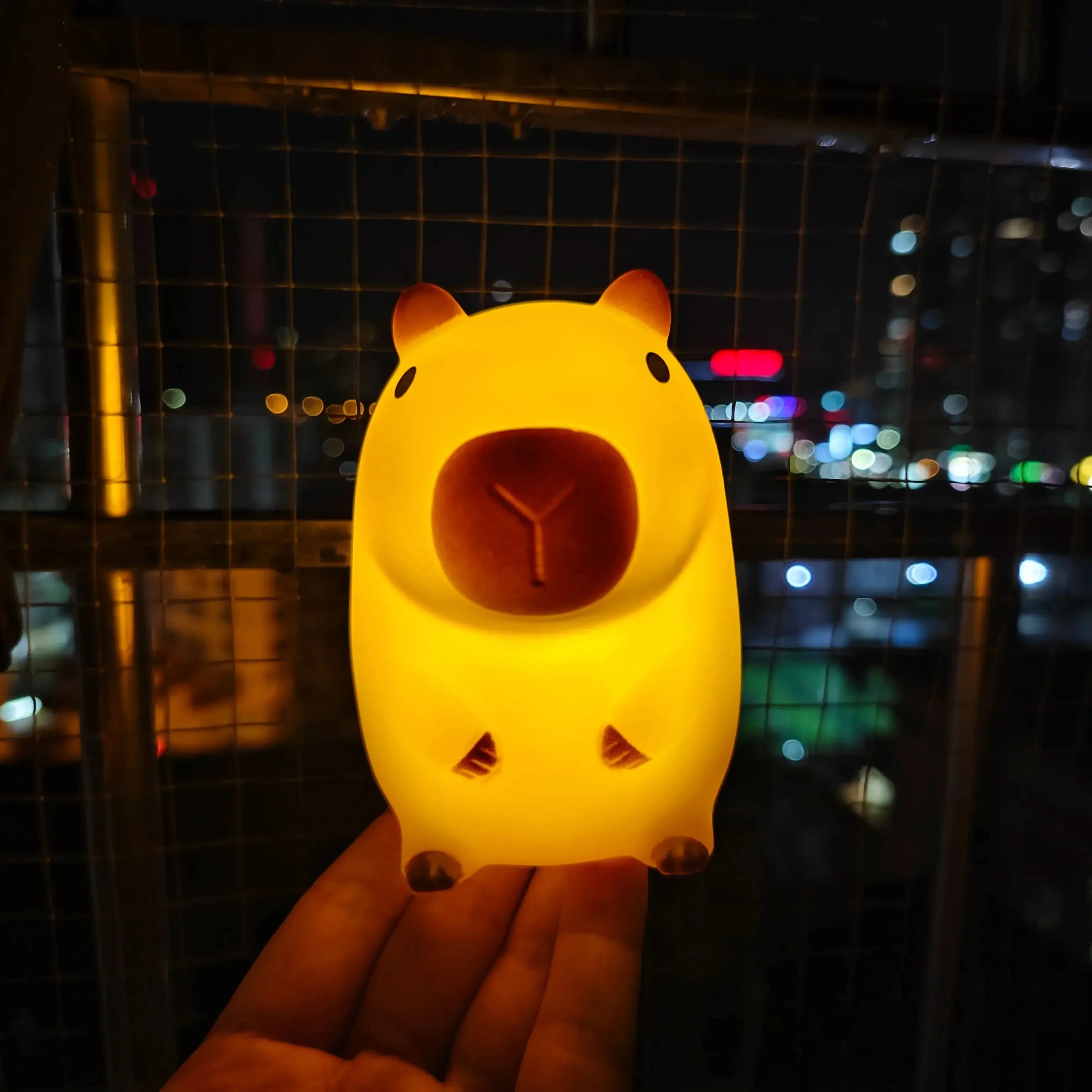 Capybara night light glowing on a hand with city lights in the background