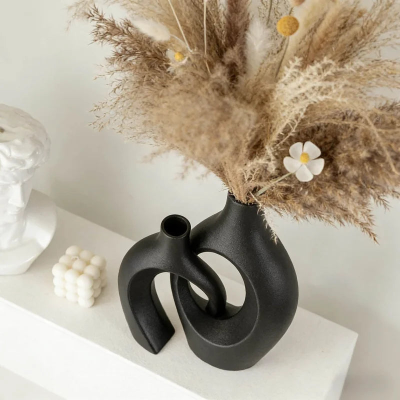 black resin vase with dried grasses and small white flowers on a display shelf