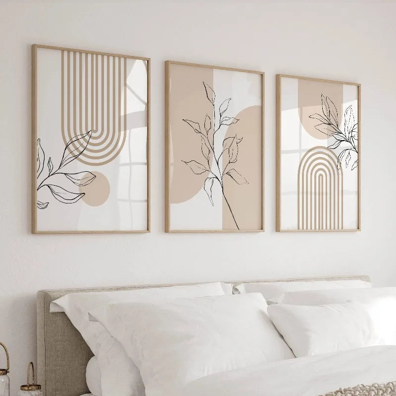 Set of three neutral botanical canvas prints in thin light wood frames above a bed with white linens