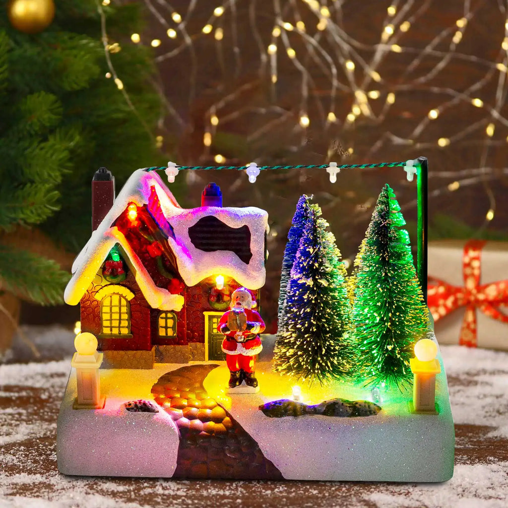 Light-up Christmas village scene with Santa, snowy house, and trees on a table
