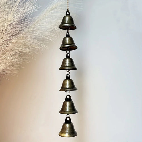 Country-style metal wind chime with six bells hanging by pampas grass on a light background