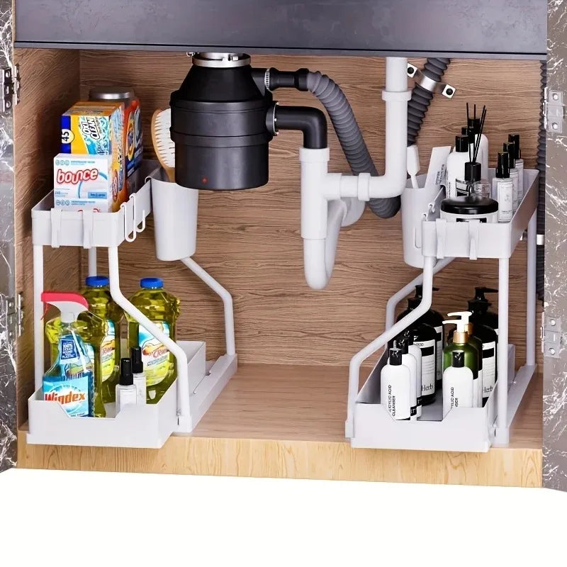 Four white under sink organizers with bottles and supplies in a cabinet with plumbing