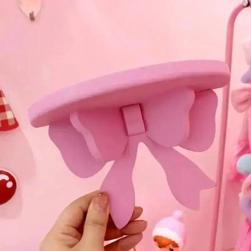 Hand holding a pink bow-shaped wooden wall shelf for girl's bedroom decor